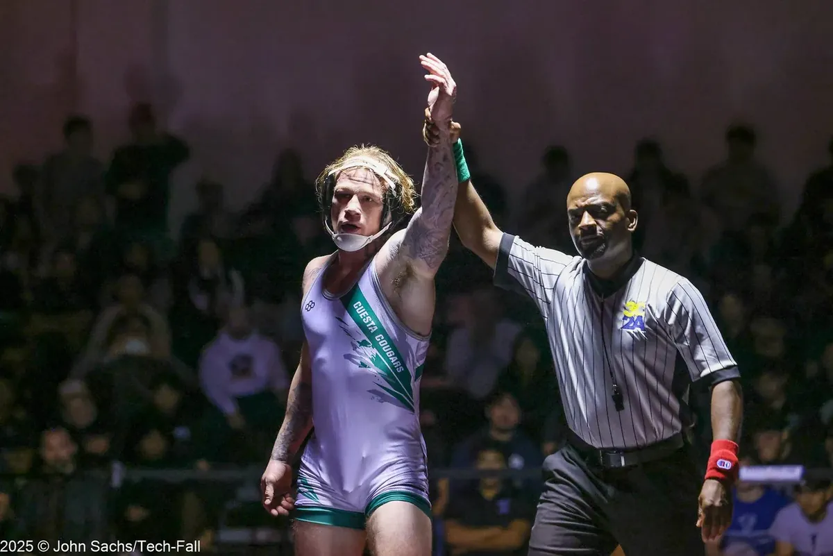 An official raises a wrestler's hand in a dark arena.
